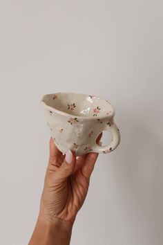 a hand holding a white cup with flowers on it