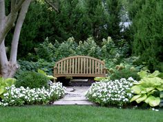 a wooden bench sitting in the middle of a lush green park filled with flowers and trees