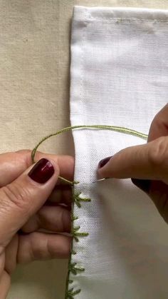 two hands are working on the edge of a piece of white fabric with green thread