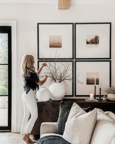 a woman standing in front of a living room with pictures on the wall behind her