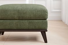 a green ottoman sitting on top of a hard wood floor next to a white wall