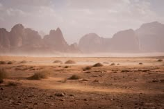 an empty desert with mountains in the background and dust blowing from the ground around it