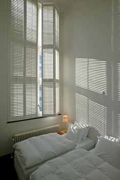 two white beds sitting next to each other in a room with windows covered in blinds