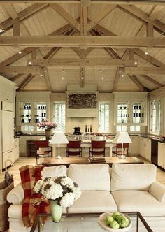 a living room filled with white furniture and lots of wood flooring next to an open kitchen