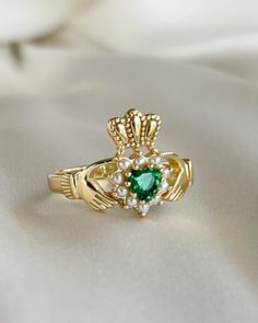 a close up of a ring on a white cloth with pearls and an emerald stone