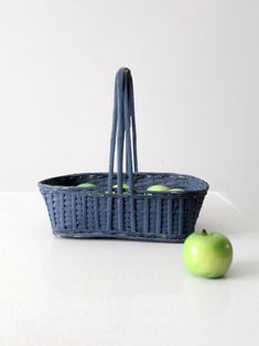 an apple sitting next to a blue basket with two apples in it on a white surface