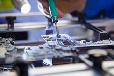 a person using a soldering tool on a piece of electronic circuit board in a factory