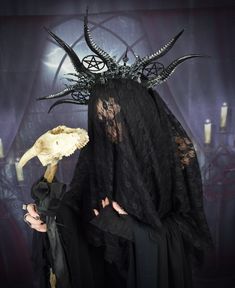 a woman in black dress holding a skull with horns on it's head and wearing a veil