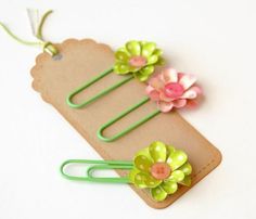 three green clips with flowers on them sitting on a piece of paper that is attached to a clip