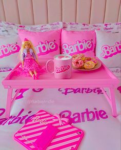 a barbie doll is sitting on a pink table with donuts and coffee mugs