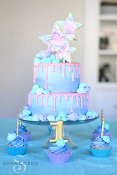 there is a blue and pink cake with stars on the top, cupcakes below it