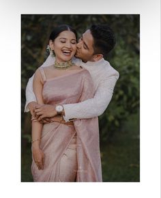 a man and woman embracing each other while standing next to each other with trees in the background