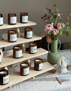 several jars of candles are arranged on a wooden shelf next to a vase with flowers