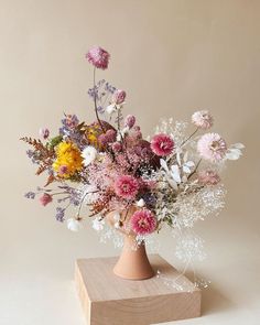 a vase filled with lots of flowers on top of a wooden block