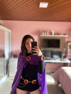 a woman in a costume taking a selfie with her cell phone while wearing a purple cape