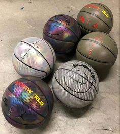 four basketballs are sitting on the floor with different colors and logos painted on them