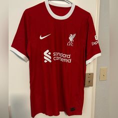 a red shirt hanging on a door with the liverpool fc logo on it and white letters