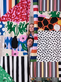 two people peeking out from between colorful fabrics