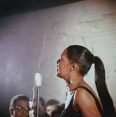 a woman singing into a microphone in front of a group of people at an event