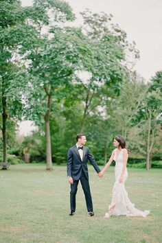 a bride and groom holding hands in the grass with trees behind them at their wedding