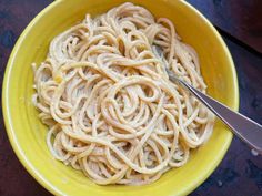 a yellow bowl filled with pasta on top of a wooden table next to a fork