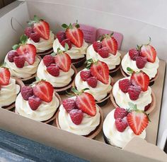 a box filled with cupcakes covered in white frosting and topped with fresh strawberries