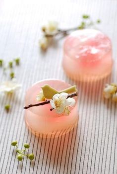 two pink cups with flowers on them sitting on a table next to some buds and twigs