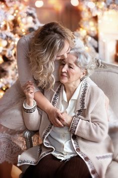 an older woman hugging her granddaughter on the lap of a chair in front of a christmas tree