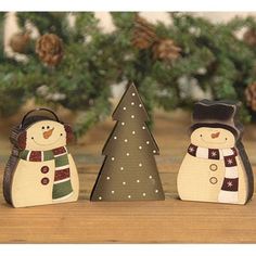 three wooden snowmen standing next to each other in front of a christmas tree and pine cones