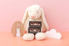 a white bunny sitting on top of a table next to a wooden sign with eyelashes