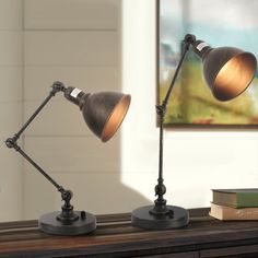 two desk lamps sitting on top of a wooden table next to a book and lamp