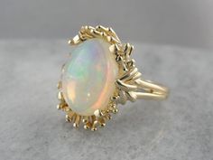 This stone has a kinetic feel, with swirling colors in the stone framed perfectly by the curving prongs and waving style of the vintage setting. The flecks inside are both pink and green, and because there is so little opacity to the stone, they shine through brilliantly. Metal: 14K Yellow Gold Gem: Opal 4.41 Carats Gem Measurements: 11.3 x 14.5 mm, Oval Ring Size: 6 Marks: "14K" Stamped on the inside band Luxury Gold Opal Ring Art Deco Style, Opulent Opal Settings Rings, Luxury Elegant Opal Ring With Stone Setting, Luxury Elegant Opal Ring With Round Stone, Luxury Vintage Opal Gemstone Ring, Luxury Opal Ring With Round Stone For Formal Occasions, Luxury Vintage Crystal Ring, Luxury Vintage Round Crystal Ring, Luxury Classic Opal Ring