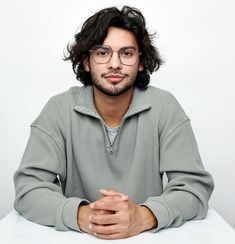 a man sitting at a table with his hands folded in front of him and wearing glasses