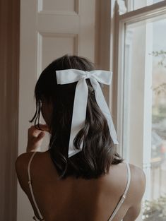 a woman with a white bow on her head looking out a window at the street