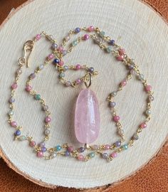 "This soft pastel colored multi Sapphire necklace featuring a stunning centerpiece, a large peachy pink Morganite pendant, captures the essence of the season, radiating femininity. The large, smooth polished natural pink Morganite pendant measures 2.2 x 1.1 cm. This alluring gemstone is suspended from a 19.5\" (50 cm) long multicolor Sapphire rosary chain, fastened by a hand forged 14k gold filled hook clasp. The sparkly multi Sapphire rosary chain boasts a luxurious 22k gold vermeil finish. The Pink Gold Gemstone Pendant Necklace, Pink Gold Pendant Necklace With Gemstone, Pink Morganite Jewelry With Gemstone Accents, Pink Morganite Gemstone Jewelry, Pink Delicate Necklace With Gemstone Beads, Delicate Pink Gemstone Bead Necklaces, Delicate Pink Gemstone Beaded Necklaces, Delicate Pink Gemstone Beads Necklace, Delicate Pink Gemstone Crystal Necklace