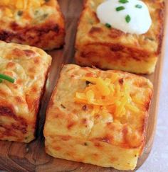 several square pieces of food on a wooden tray with cheese and sour cream toppings