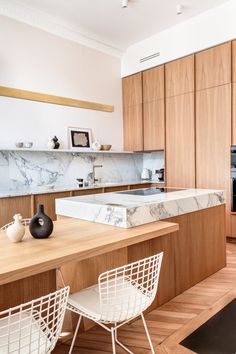 a modern kitchen with marble counter tops and wooden cabinetry, along with white chairs