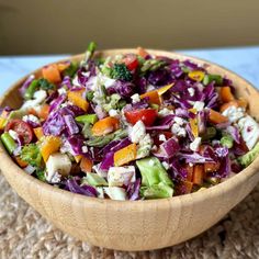 a wooden bowl filled with salad on top of a table next to a blue cloth