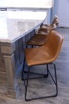 three leather chairs sitting on top of a kitchen counter next to a marble topped island