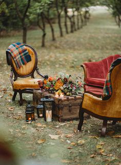 two chairs and a table with flowers on it in the grass next to some trees