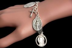 "A Miraculous Medal combined with a collection of silver plated Christian theme charms have been dispersed around a shimmering silver plated bracelet chain in this handmade charm bracelet. This religious charm bracelet is then completed with a lobster clasp and a 1/2 inch of chain at the end for adjustable sizing. ● Bracelet Styles ● Style #1 - Charms in this bracelet include a \"Christ Carrying the Cross\" charm, praying hands charm, a \"So Very Blessed\" charm, a Jesus fish charm, a \"Jesus lo Saint Peregrine, Christ Carrying The Cross, Saint Mary Magdalene, Carrying The Cross, St Peregrine, Saint Necklace, Maria Goretti, Catholic Bracelet, St Maria