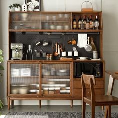 a wooden cabinet with glass doors and shelves filled with kitchen utensils next to a dining room table