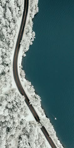 an aerial view of a winding road in the middle of snow covered trees and water