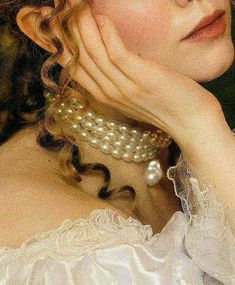 a woman in a white dress with pearls on her neck and hands near her face