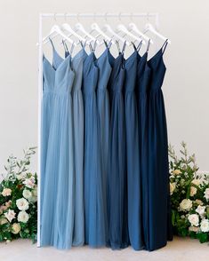 four bridesmaid dresses hanging on a rack in front of flowers