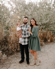 a man and woman holding a baby standing in front of some bushes at the beach