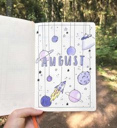 a hand holding an open notebook with the words august written in space and planets on it