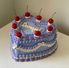 a cake with blue icing and cherries sitting on top of a white table