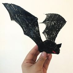 a hand holding up a piece of black string art that looks like a dragon's wings