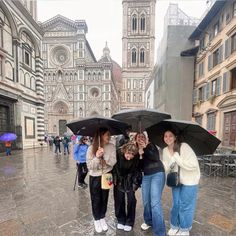 three women are standing under umbrellas in the rain on a city street with buildings behind them